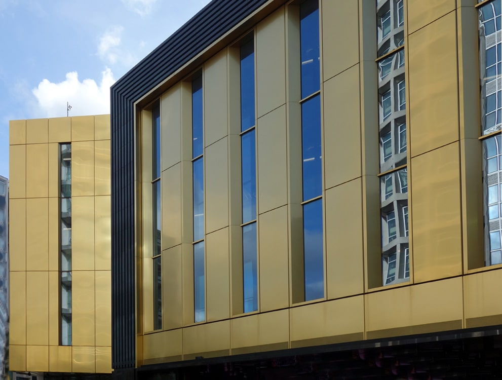 Gevelbekleding in Hairline RVS met gouden PVD-afwerking aan gebouwgevel