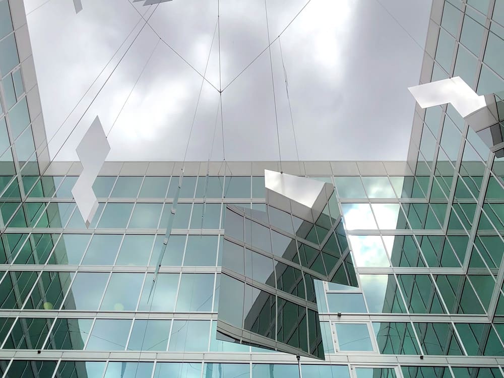 Marine Mirror 9 RVS plaat verwerkt in hangende kunstinstallatie tussen kantoorgebouwen