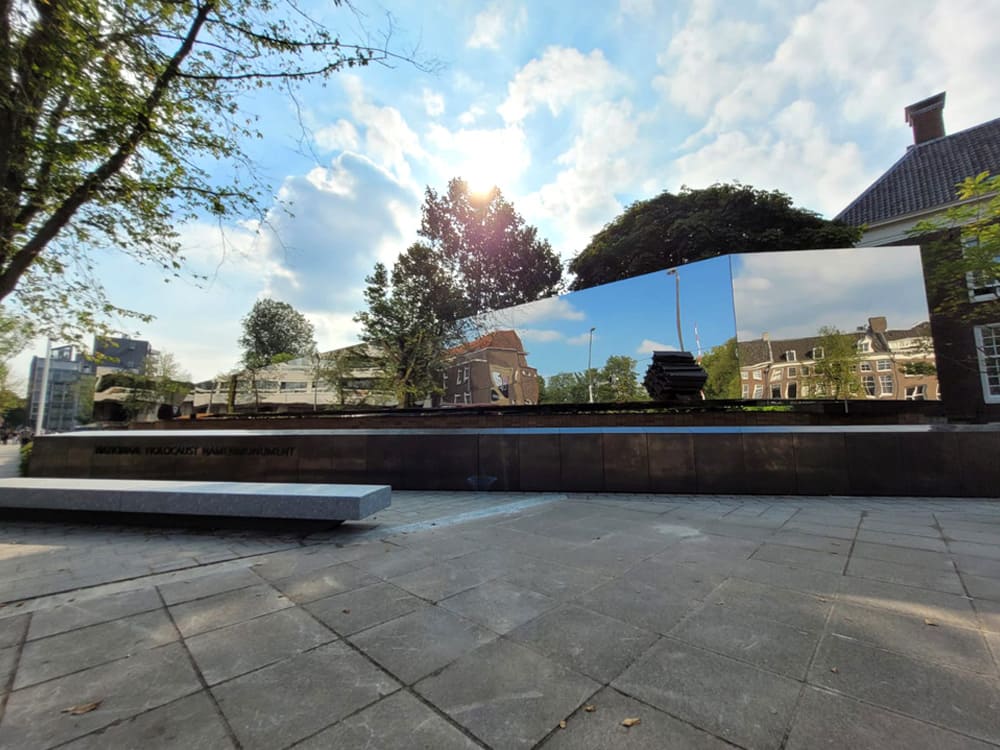 Spiegelende RVS-wand van het Nederlands Holocaust Namenmonument in Amsterdam, reflecteert de omliggende grachtenpanden