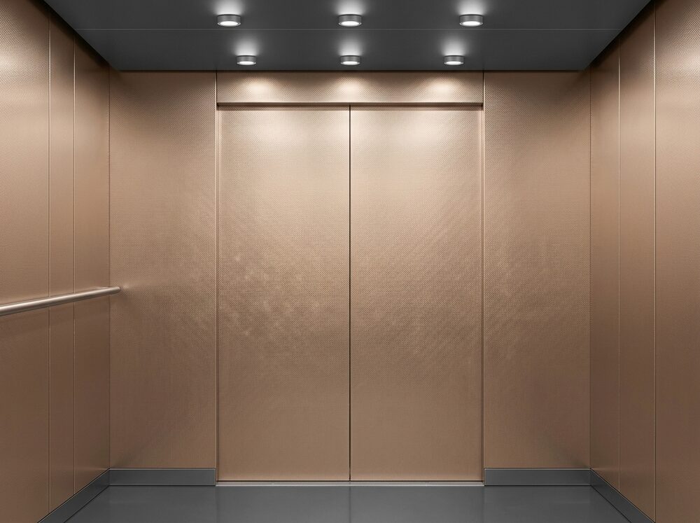 Liftcabine met wandpanelen van RVS met een fijn geweven linnenmotief in een roségouden tint